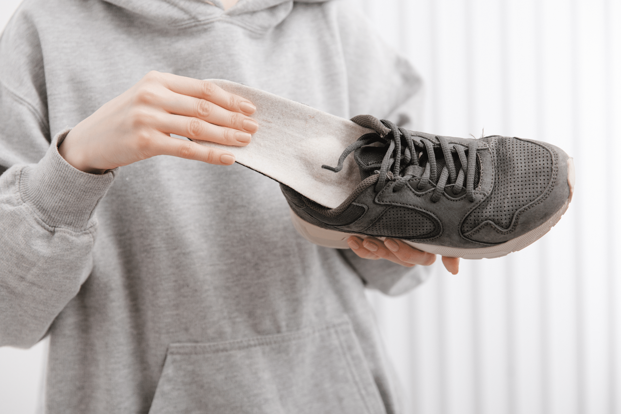 Fitness woman in sportswear with orthopedic insoles and sneakers. Woman putting orthopedic insole into shoe at home close up. Foot care banner. Flat Feet Correction.