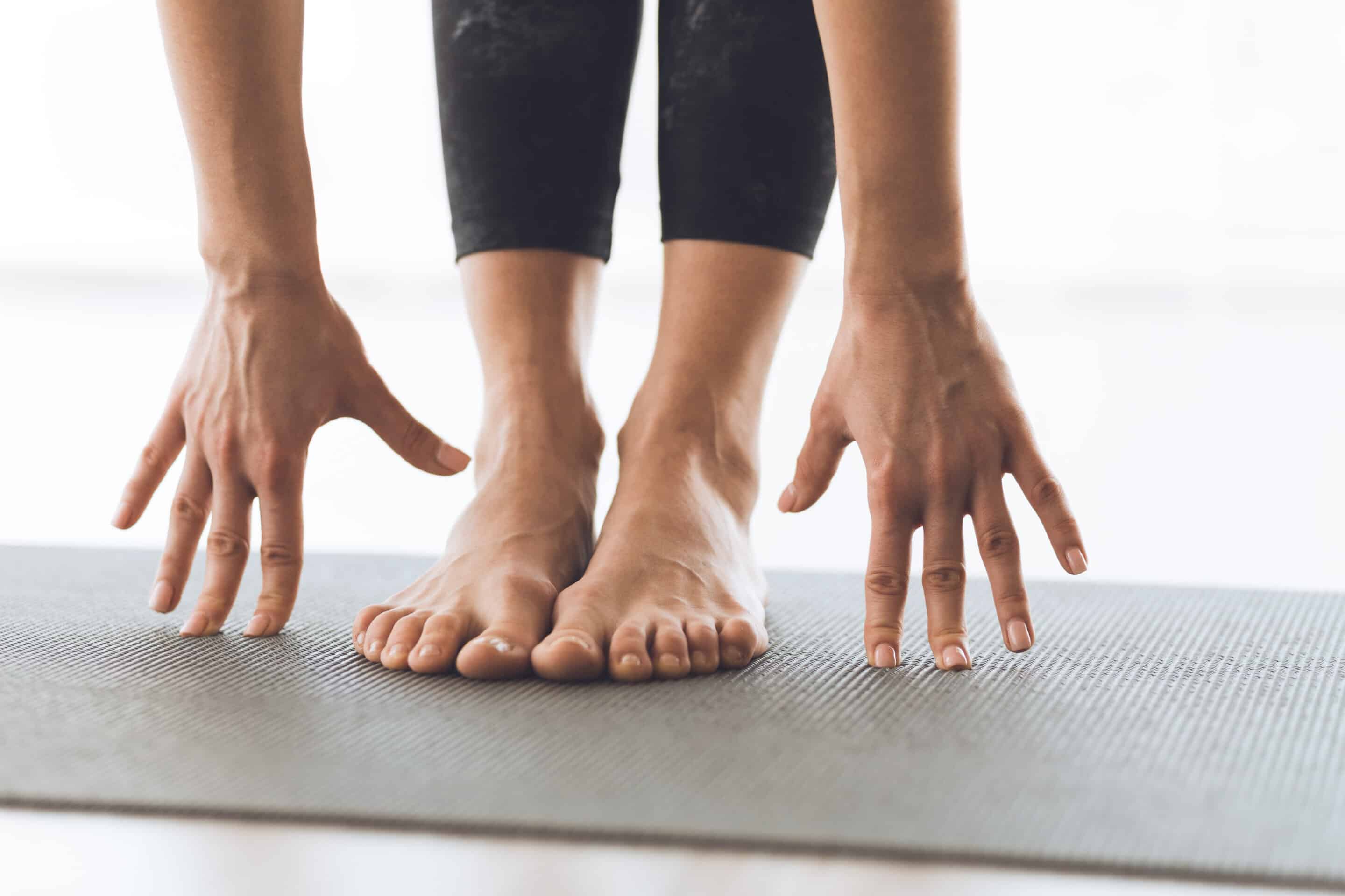 Relax Concept. Close up of girl's hands and feet during yoga classes. Young slim girl making exercise indoor on gray mat